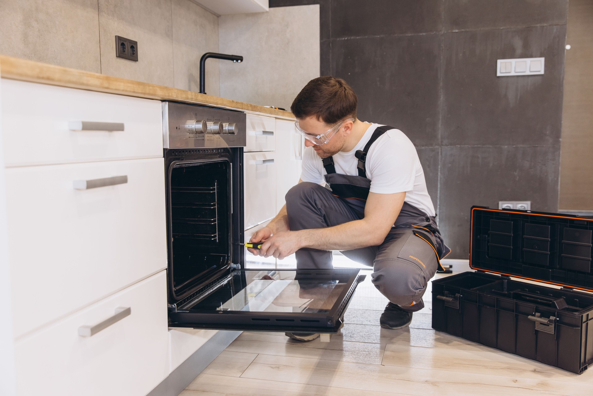 Professional plumber repairing oven in a modern kitchen